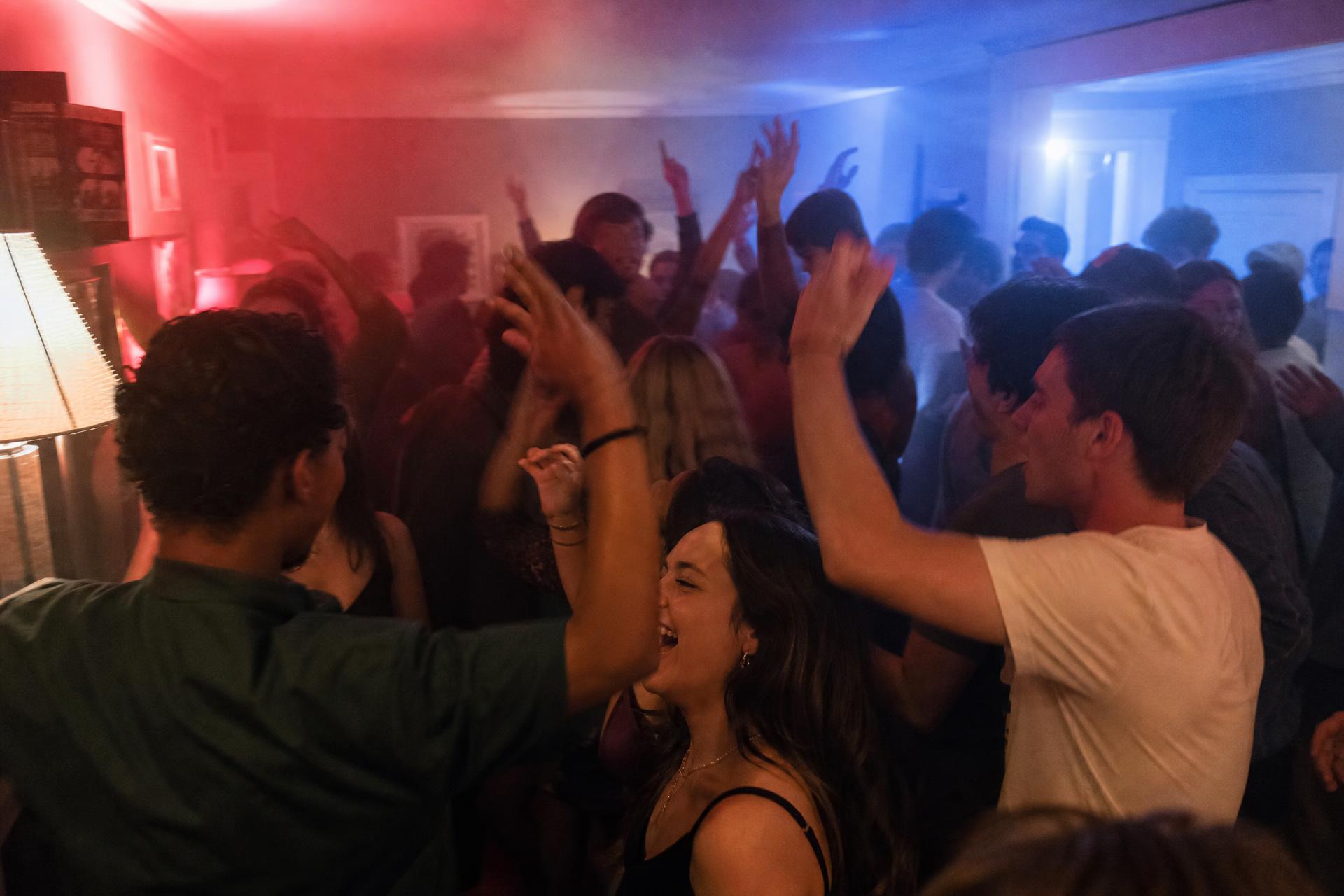 Students dancing with their hands up in coloured light at a house party